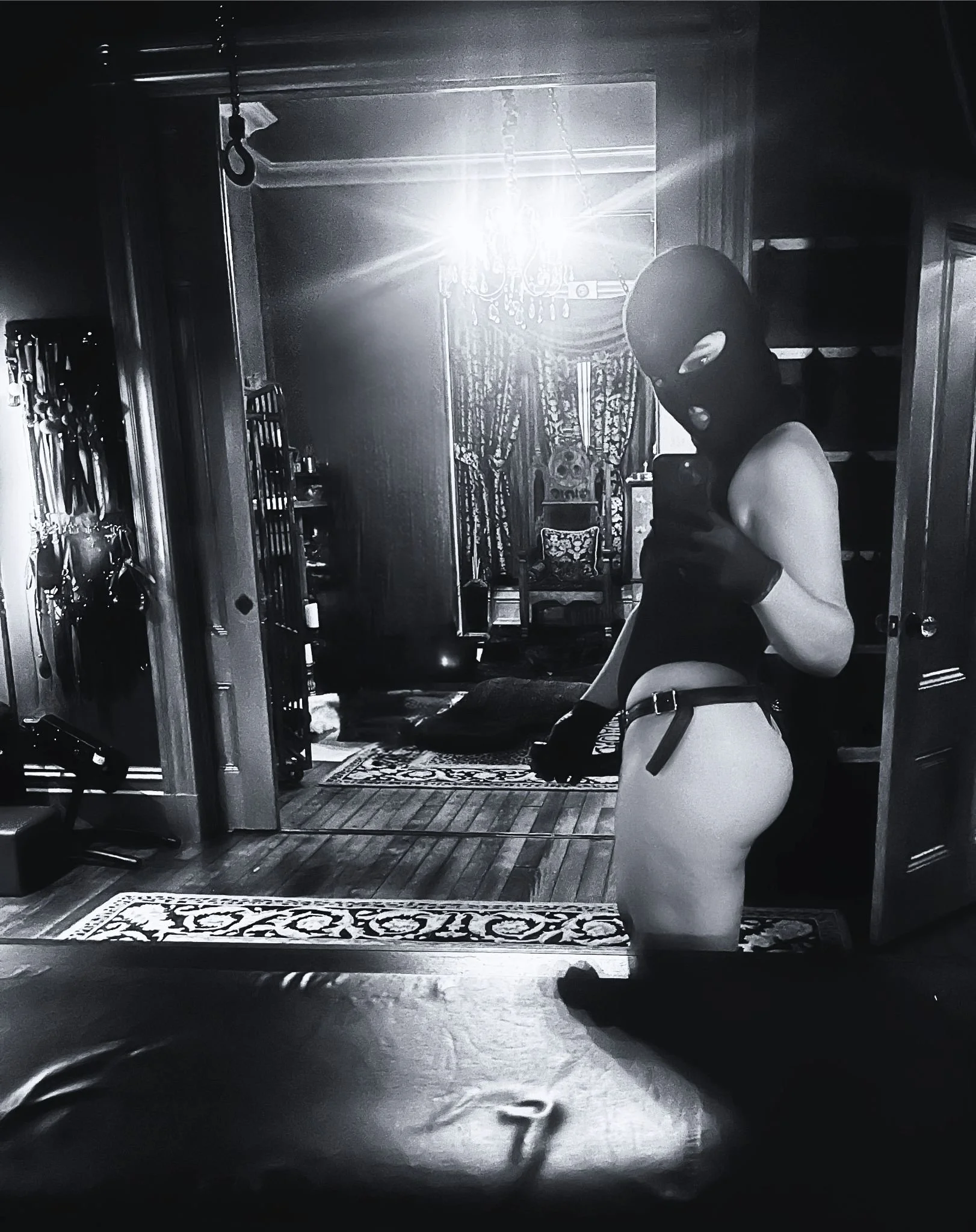 San Francisco Dominatrix in a ski mask, taking a mirror selfie among vintage furniture and curtains in bright sunlight.